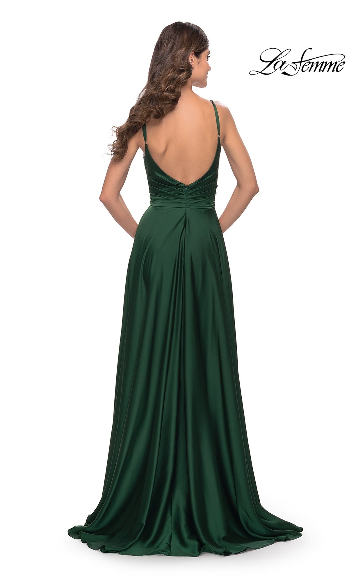 Woman in a floor-length emerald green La Femme Open-Back A-Line Designer Prom Dress 31233, featuring spaghetti straps and a deep V-back, stands with her back to the camera.